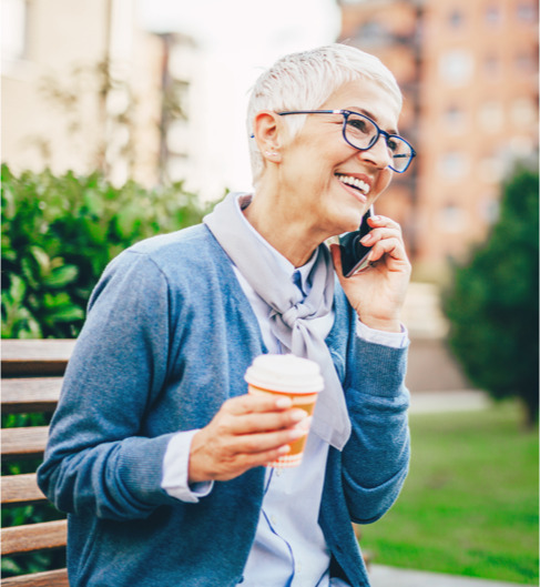 an elderly woman holds coffee in hand while talking on mobile phone