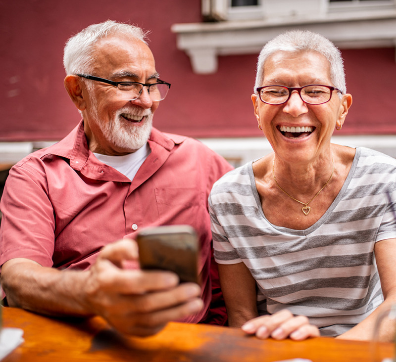 an elderly couple look at mobile phone and laugh