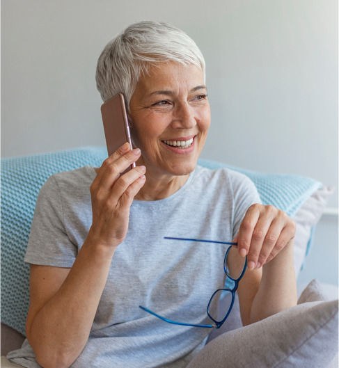 an elderly woman talks on mobile phone while holding glasses and smiling