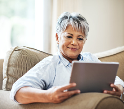 an elderly woman sits on couch and looks at tablet